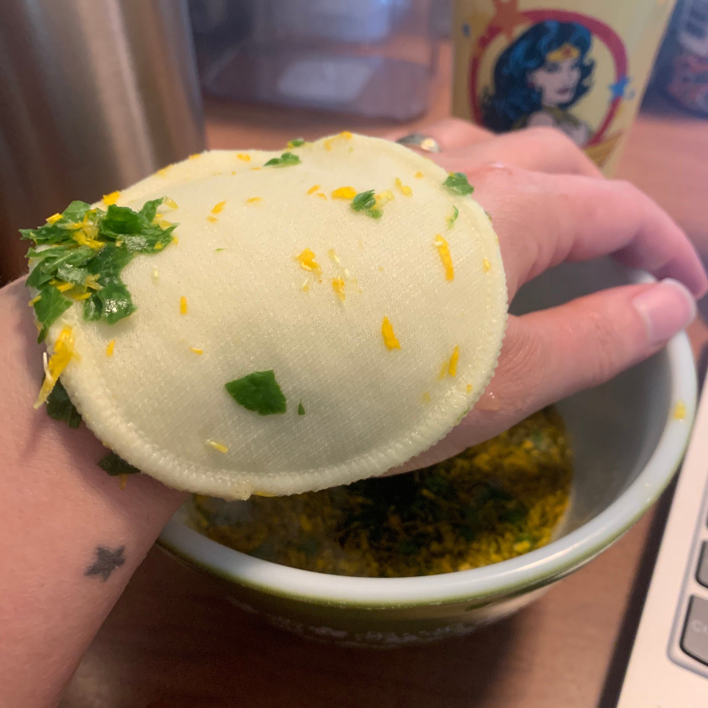 My hand with a cold herbal compress laying on top of it - a washable cotton round soaked in an herbal infusion