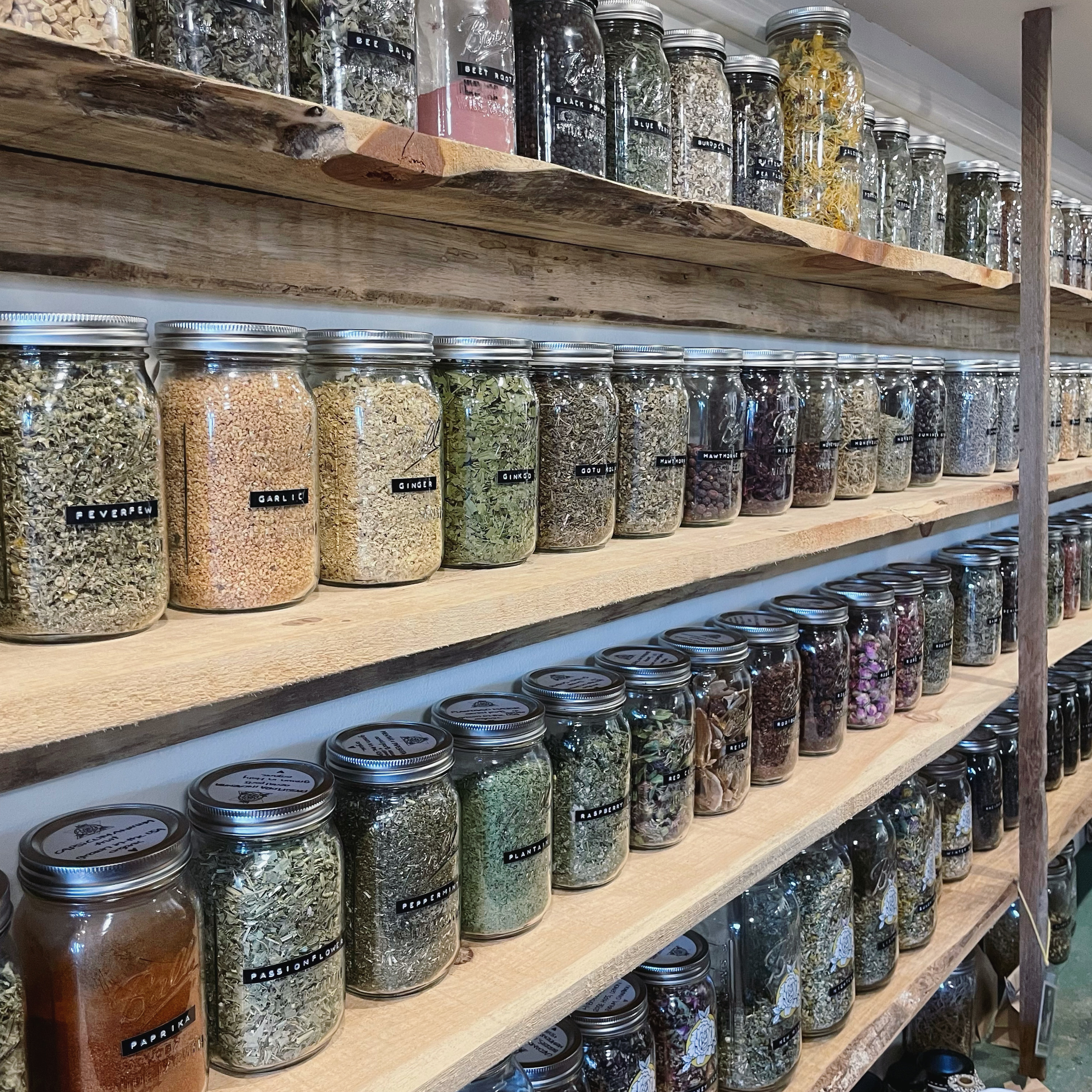 Colorful dried herbs and spices in mason jars on shelves made of reclaimed wood. Herbs are in alphabetical order and labeled with small black and white labels.